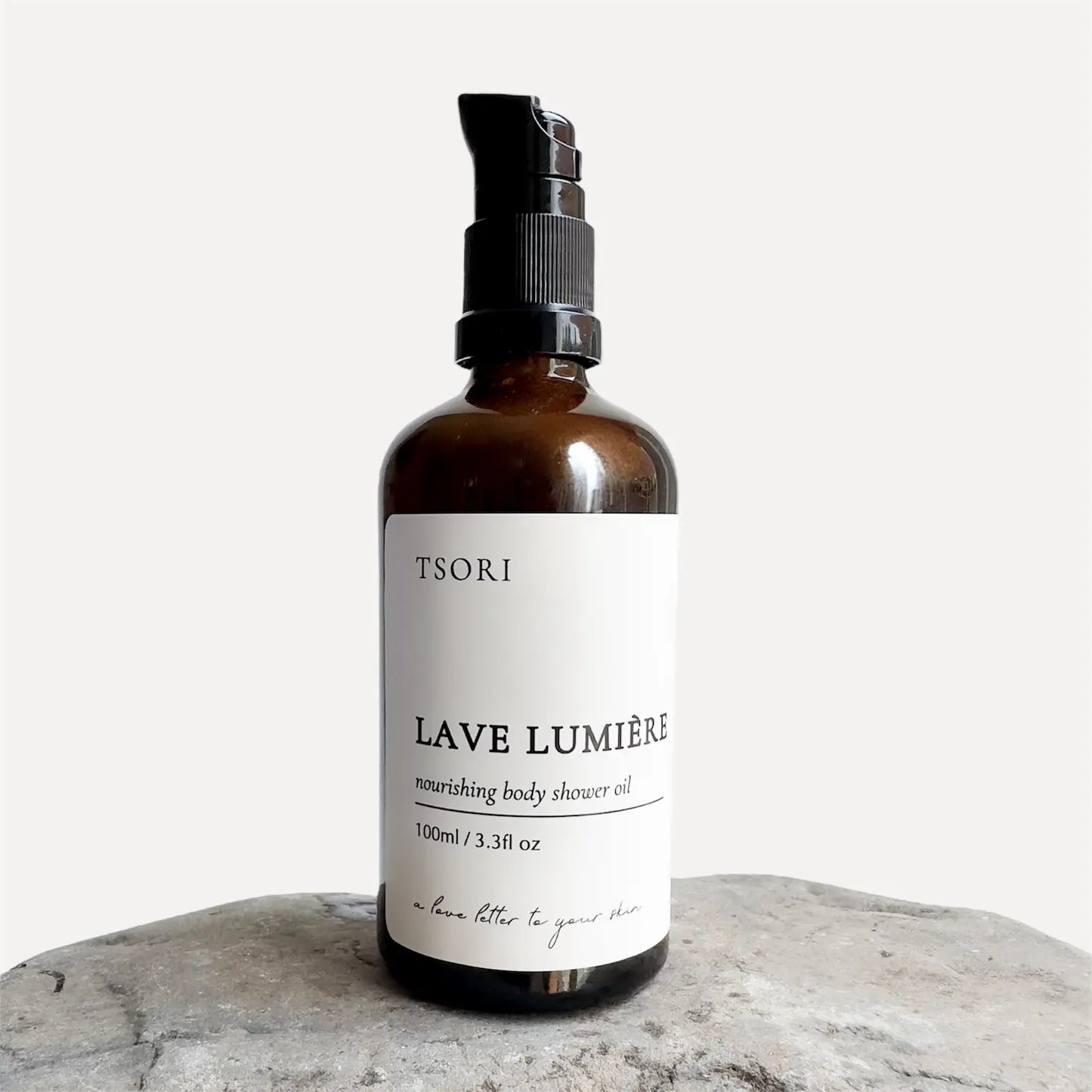 Bottle of TSORI Lave Lumiere body shower oil on a stone surface with a white background