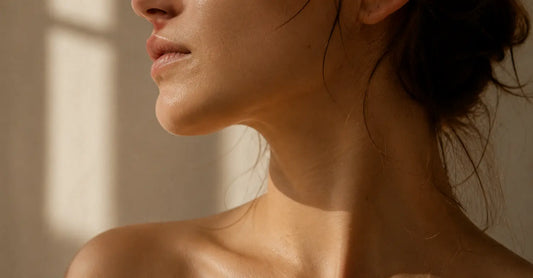 Close-up of a woman’s bare jaw and neck in warm natural window light, showing calm, rested skin with soft film grain and a quiet editorial mood.