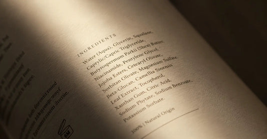 Close-up of a skincare ingredient list on an amber bottle label lit by warm natural light, with shallow depth of field and soft film grain creating a calm editorial mood.