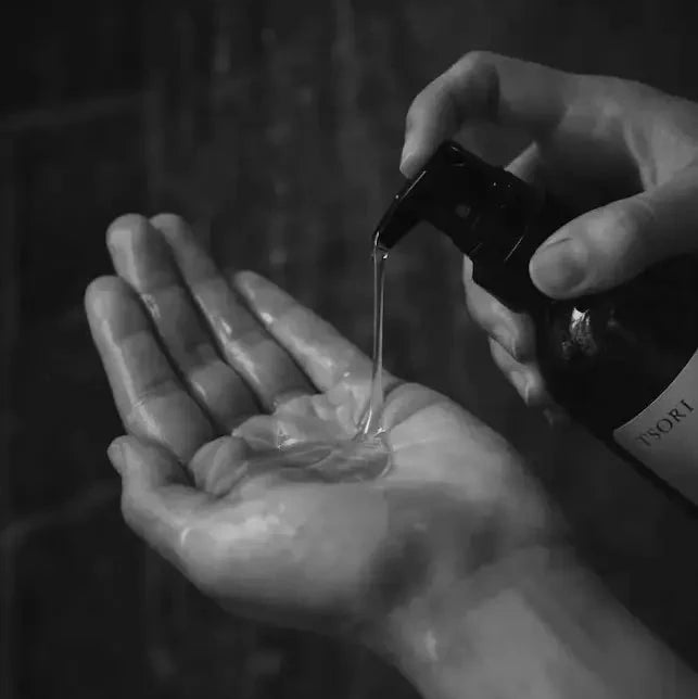 Person pouring liquid from a bottle into their hand against a dark background