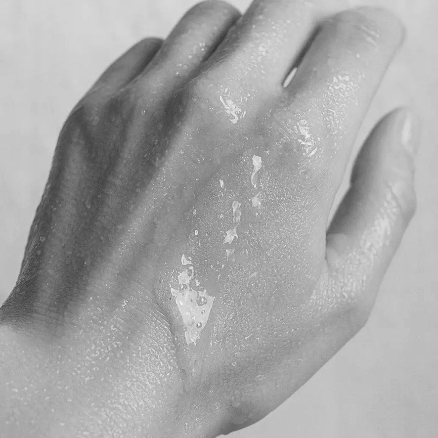 black and white image of back of hand with TSORI PSALM balm  and water drops