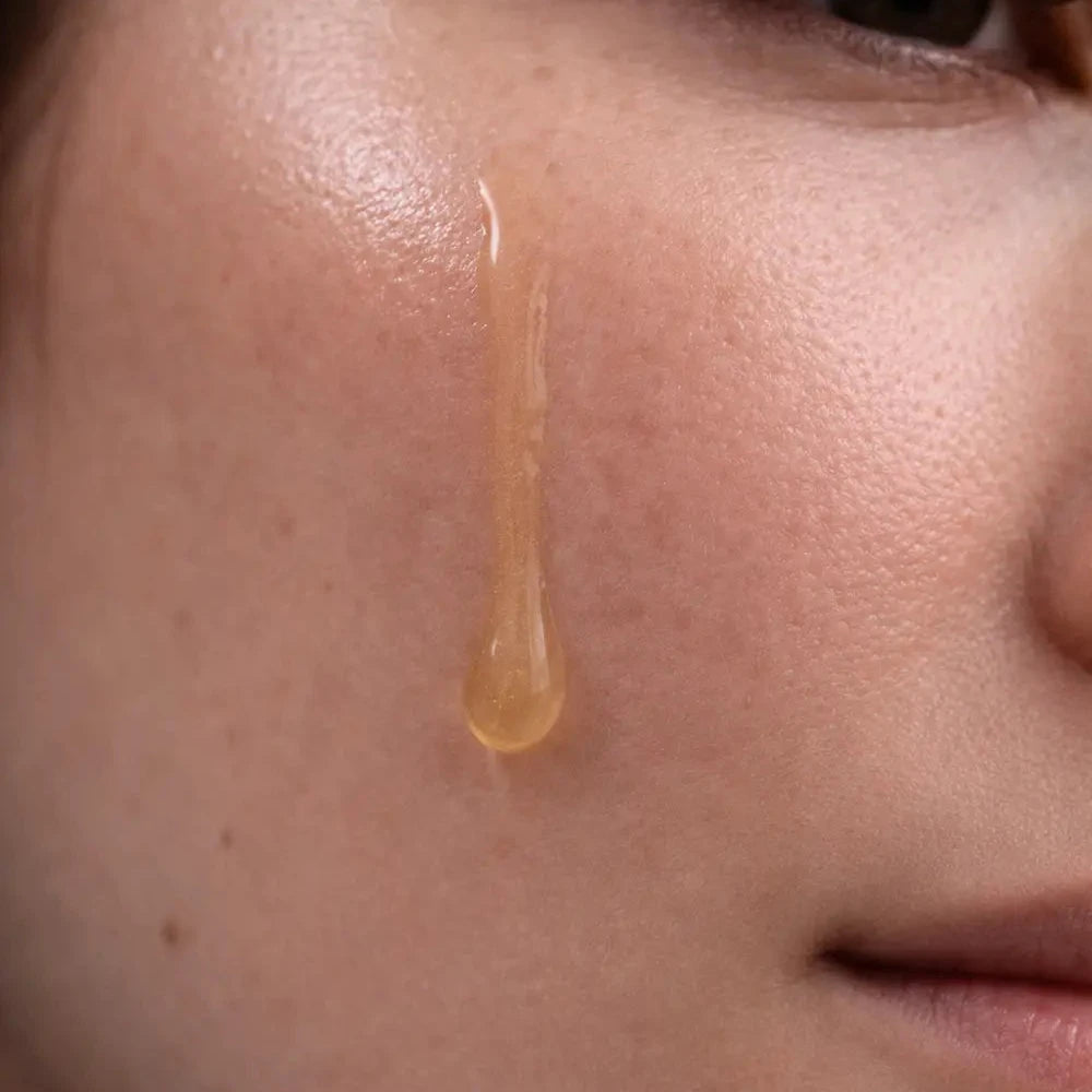 Close-up of a woman's face with a droplet of liquid on her cheek.