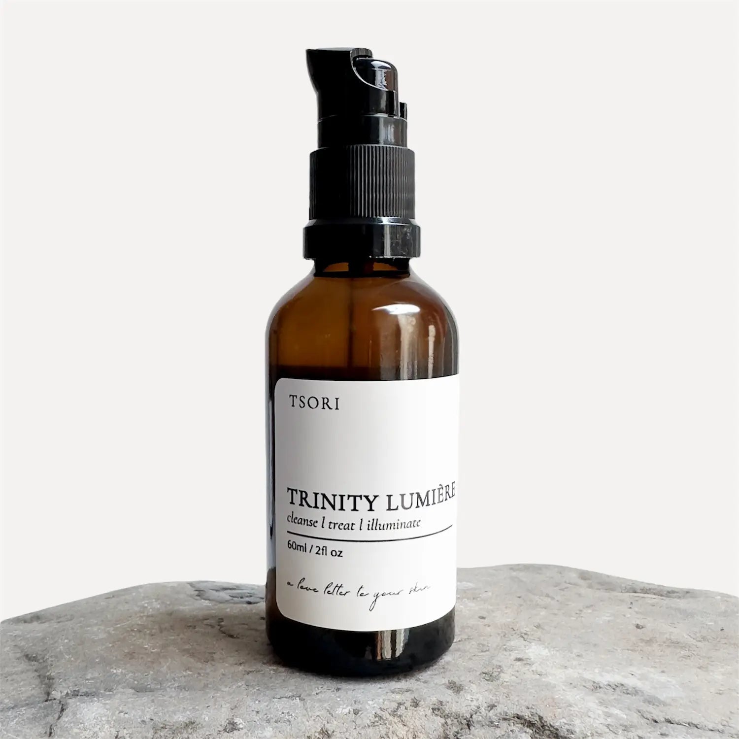 Amber bottle with black spray nozzle labeled 'Tsori Trinity Lumère' on a light gray background