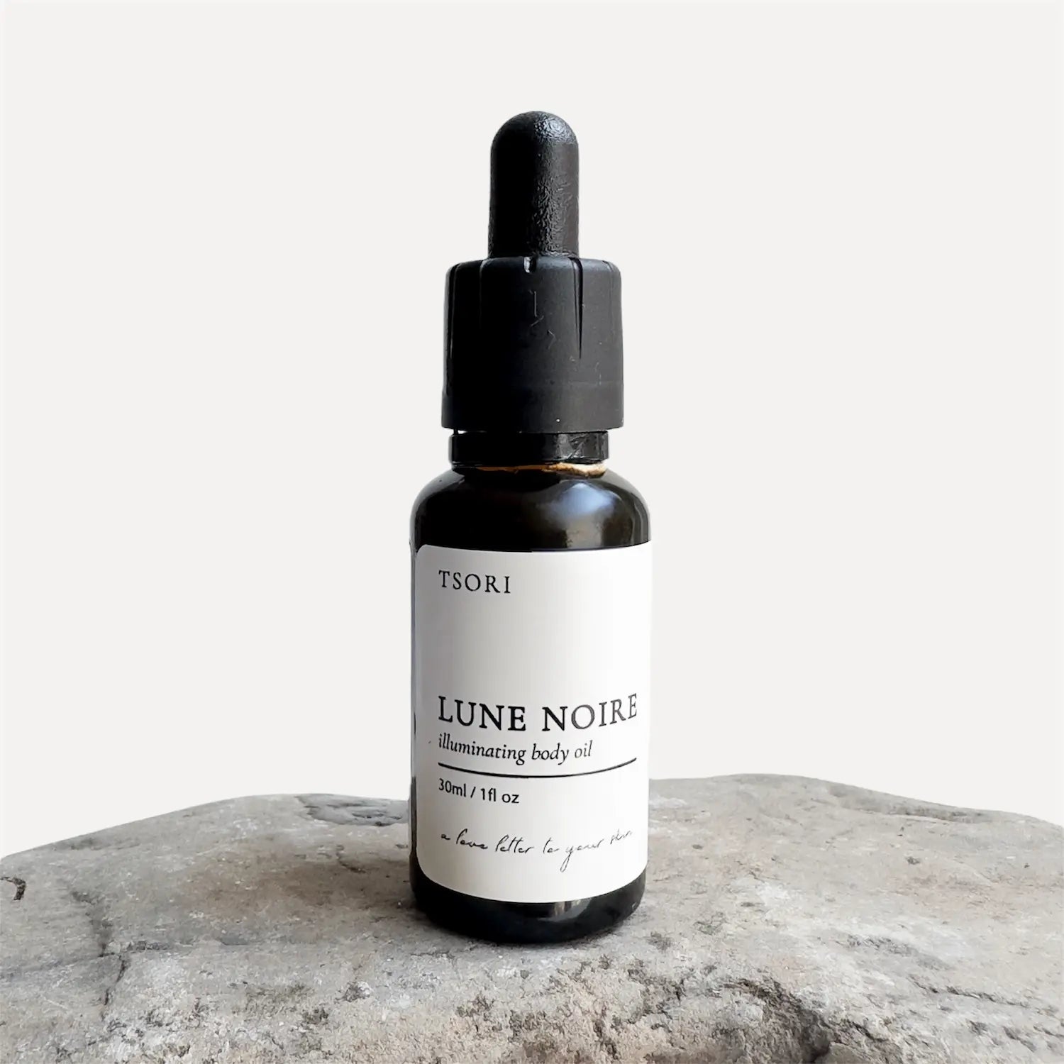 Bottle of Lune Noire illuminating body oil by Tsori on a textured surface with a white background