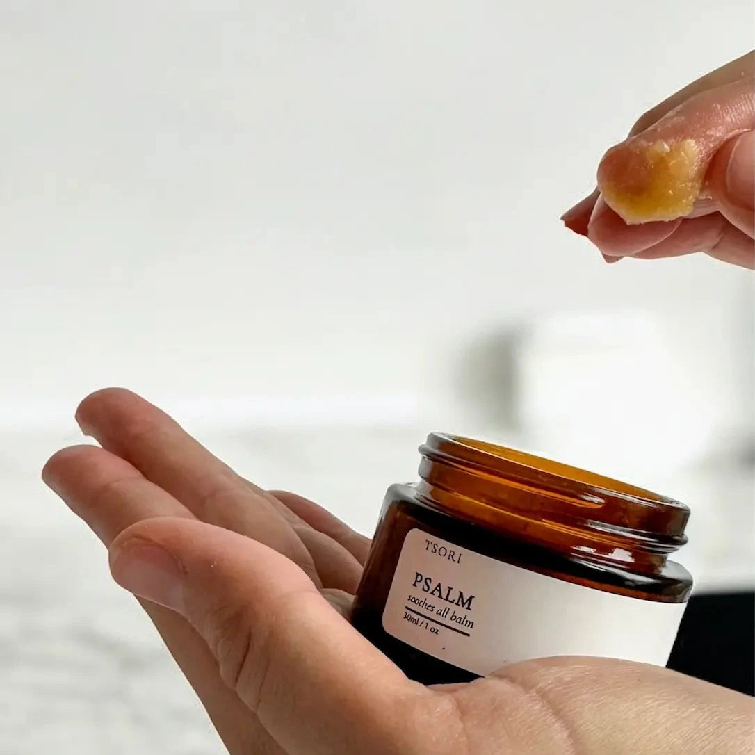 Person applying balm from a jar labeled 'Psalm' on a white background