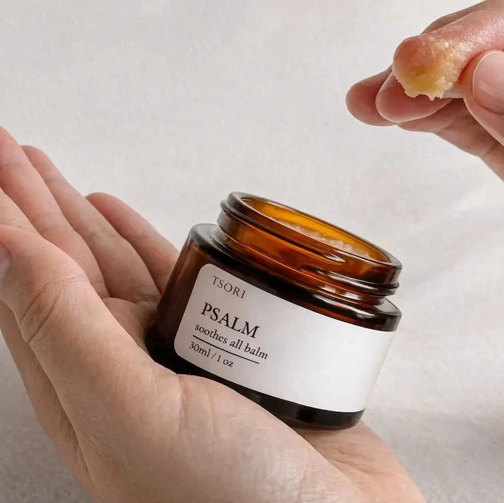 Person holding a jar of 'Psalm' balm with a small amount on a finger against a neutral background