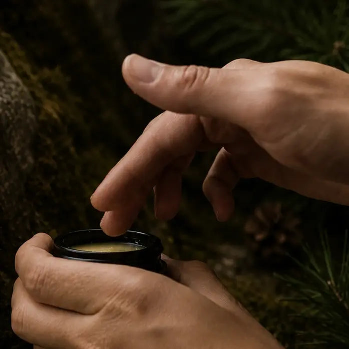 Close-up of hands holding a small black container with a green substance against a blurred natural background.